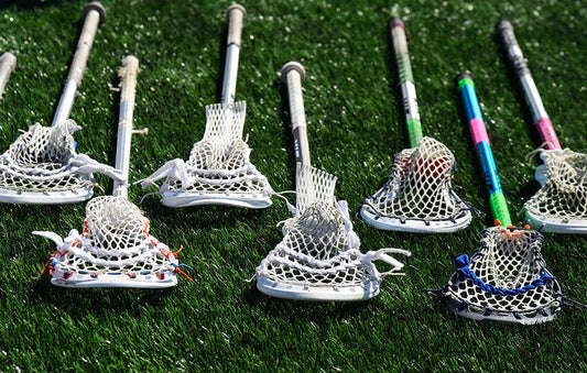 Several lacrosse sticks with mesh pockets lined up on artificial turf field.