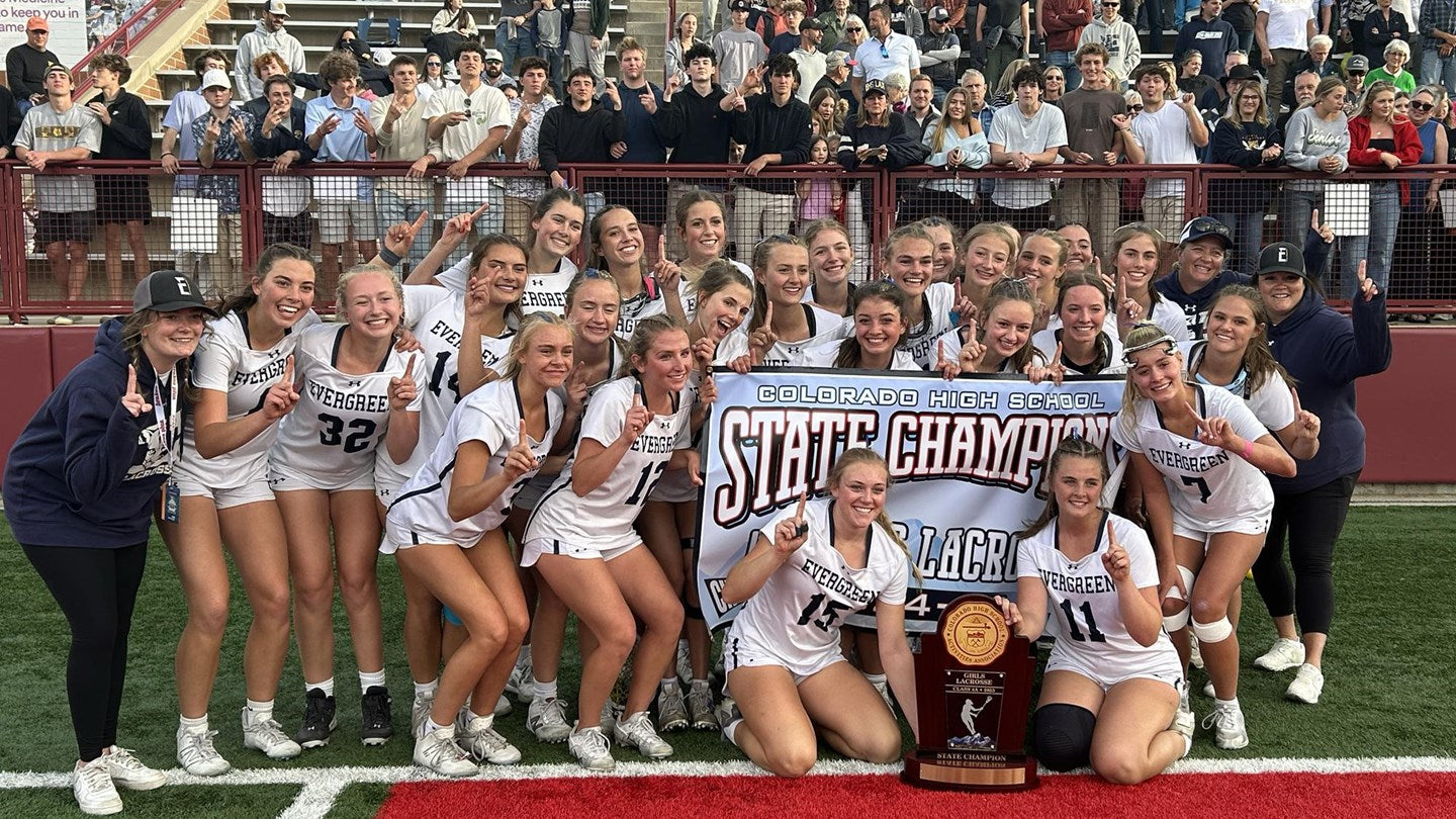 The Evergreen High School girls lacrosse team is celebrating with a state championship banner and trophy on the field.